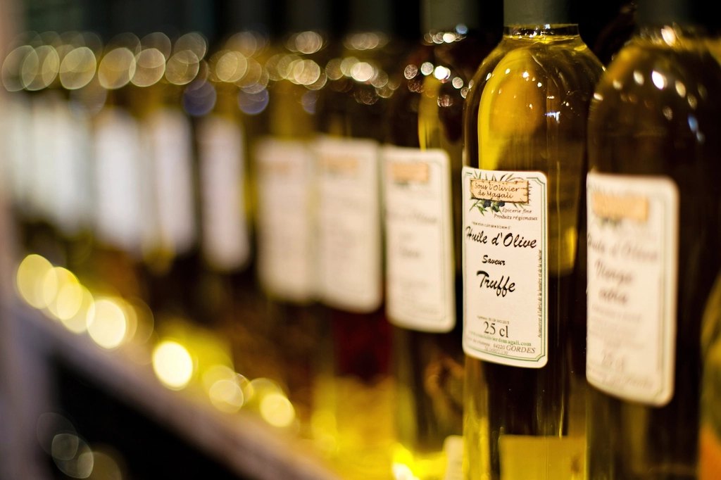 A row of olive oil bottles lined up on a shelf, lit with warm golden light