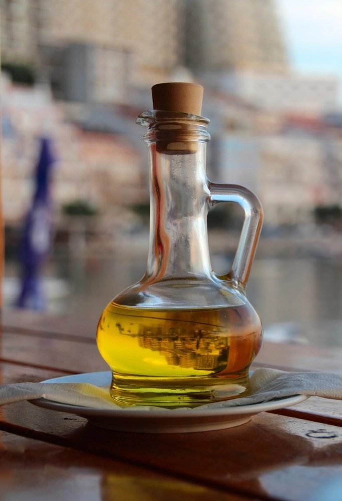 A round glass carafe filled with olive oil standing on a wooden table
