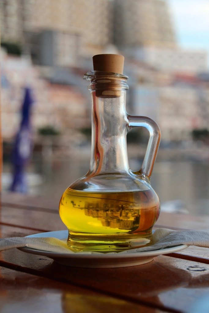 A round glass carafe filled with olive oil standing on a wooden table