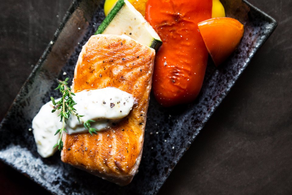 A fillet of grilled salmon served with grilled peppers and courgette on a dark plate