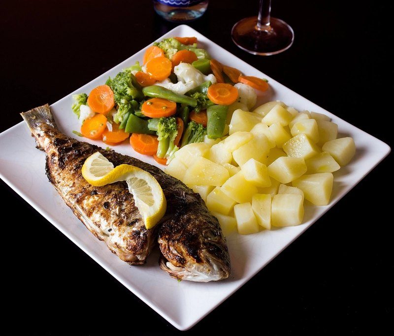 A plate of grilled whole fish with lemon, potatoes and vegetables