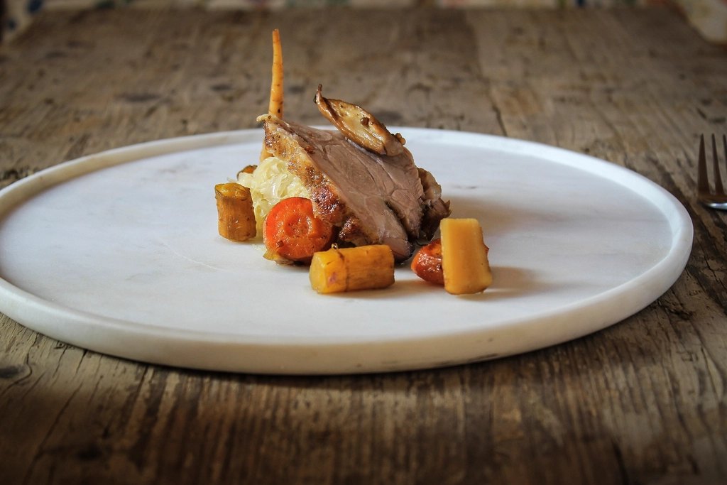 A plated portion of roast lamb with root vegetables on a round wooden board