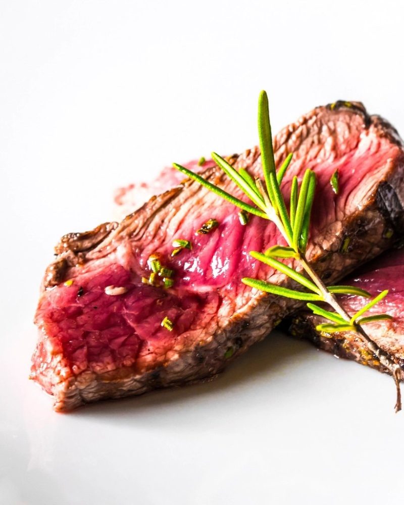 Sliced grilled beef finished with rosemary and a drizzle of olive oil on a white plate
