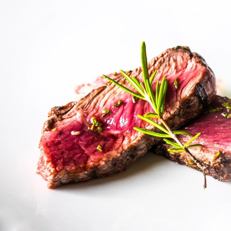 Sliced grilled beef finished with rosemary and a drizzle of olive oil on a white plate