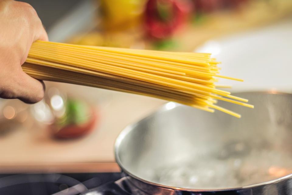 Dry spaghetti being lowered into a pan of boiling water on the stove