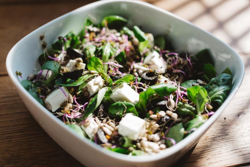 A dish of mixed leaves, sprouts and feta cheese dressed with olive oil