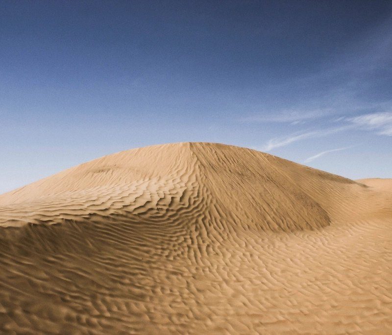 A smooth, wind-sculpted sand dune under a clear sky in southern Tunisia