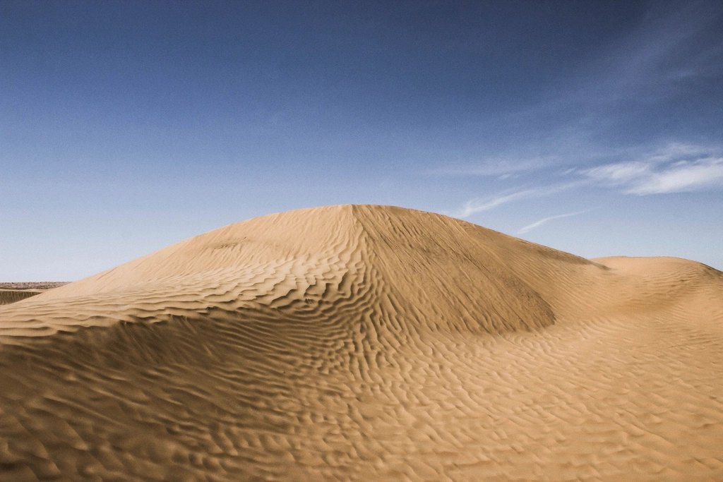 A smooth, wind-sculpted sand dune under a clear sky in southern Tunisia